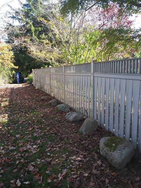 A white picket fence is surrounded by rocks and leaves in a yard.