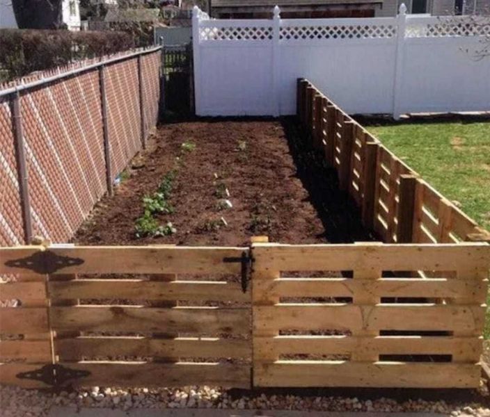 A wooden fence surrounds a garden with a white fence in the background