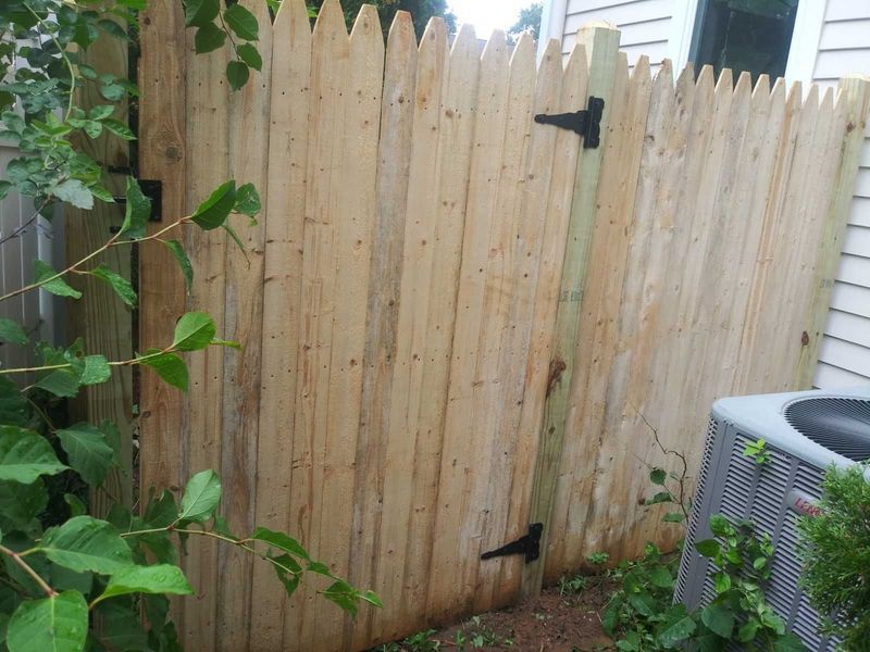A wooden fence with a gate in the backyard next to a house.