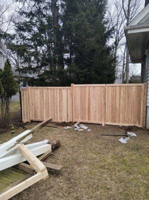 New wooden fence in a backyard. Brown planks are constructed in panels. Construction debris lies in front.