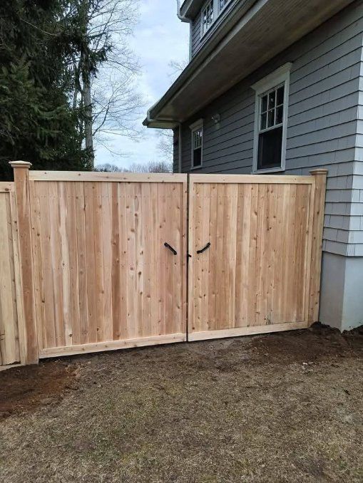Wooden double gate, light brown, next to a gray house.