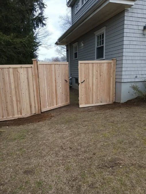 Wooden fence with open gate next to a house with gray siding.