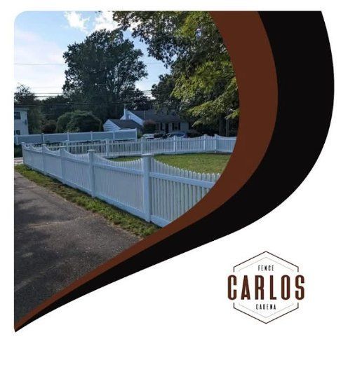 White picket fence surrounding a yard along a road, Carlos Fencing logo.