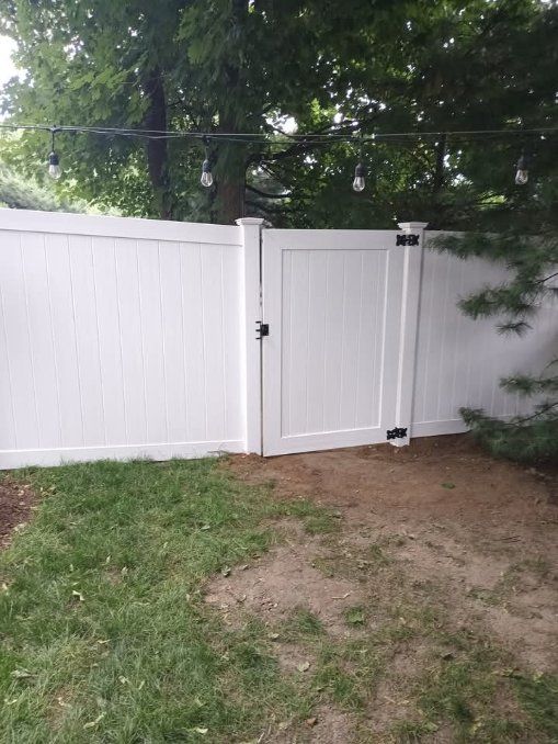 White vinyl fence with a matching gate in a yard with grass and trees.