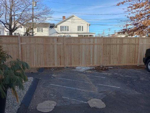 Wooden fence in a parking lot, with a house in the background. Sunny day.