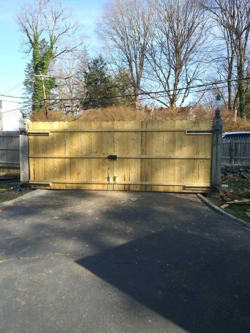 Wooden driveway gate, closed, with stone columns, asphalt driveway.