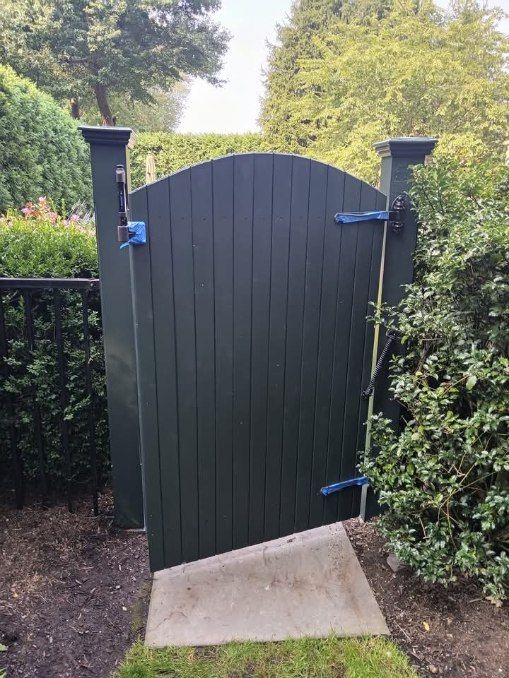 Dark green wooden gate with blue hardware, leading to a garden path.
