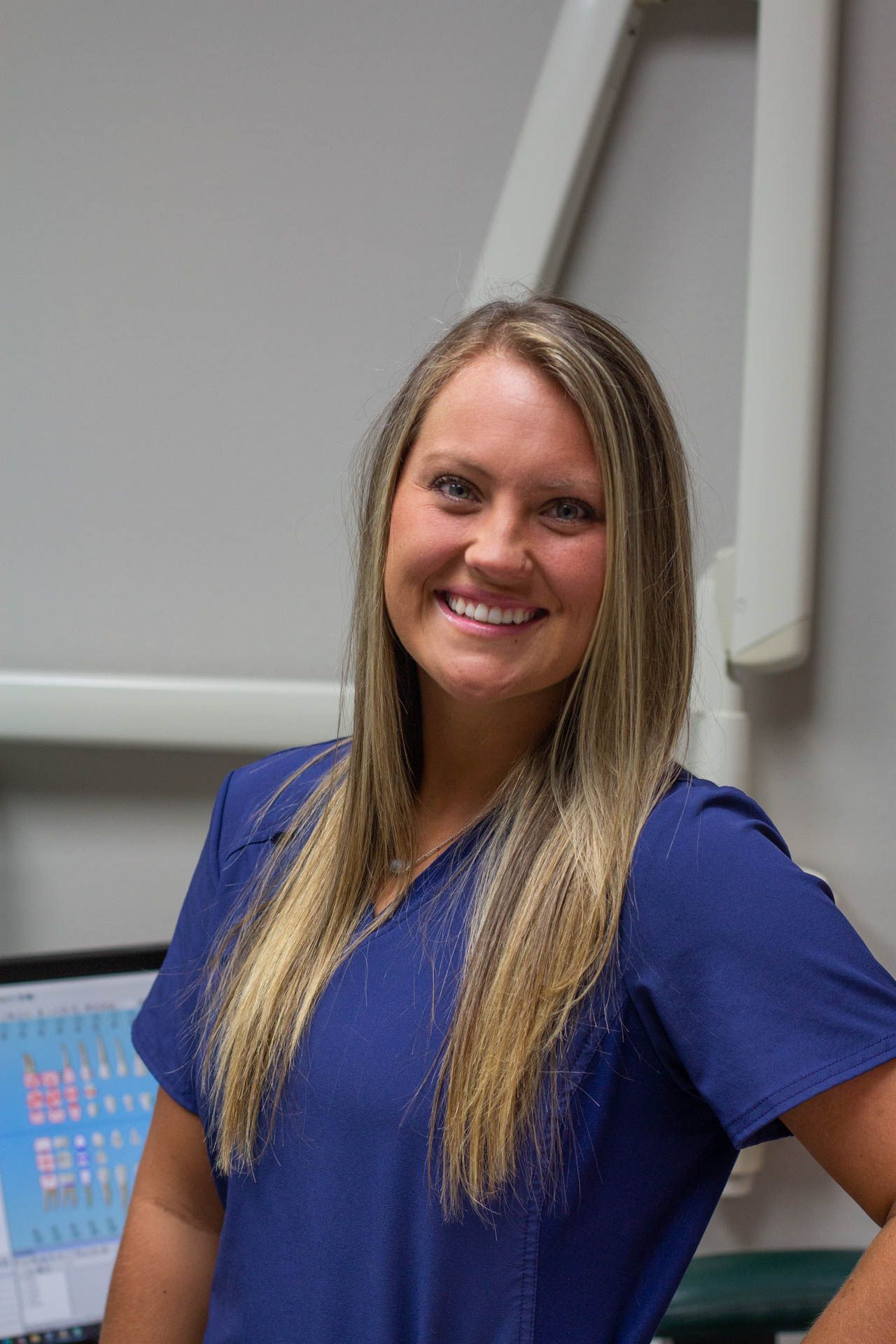 A woman in a blue scrub top is smiling for the camera.