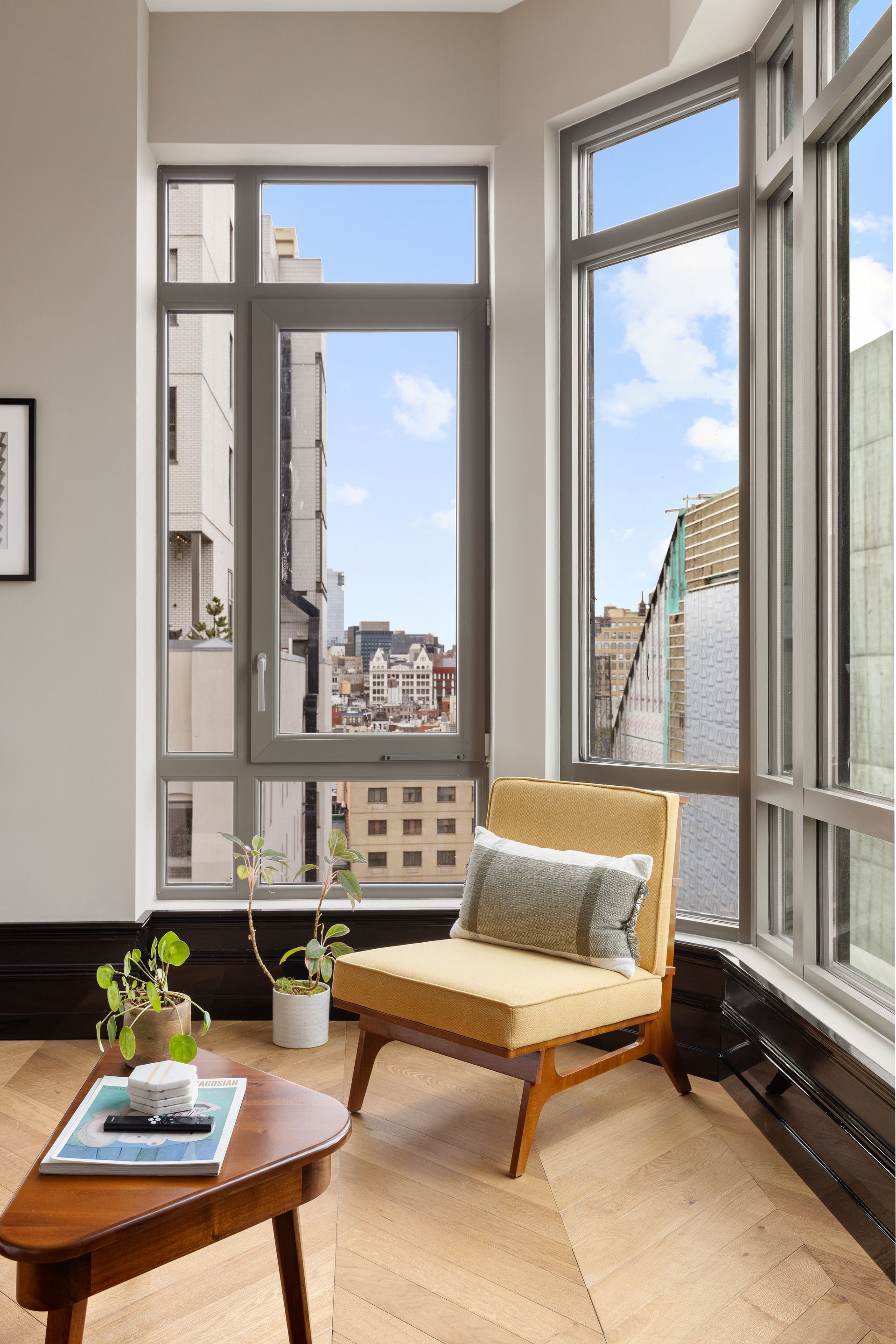 Cozy corner with yellow chair and small table by a tall window overlooking city buildings.