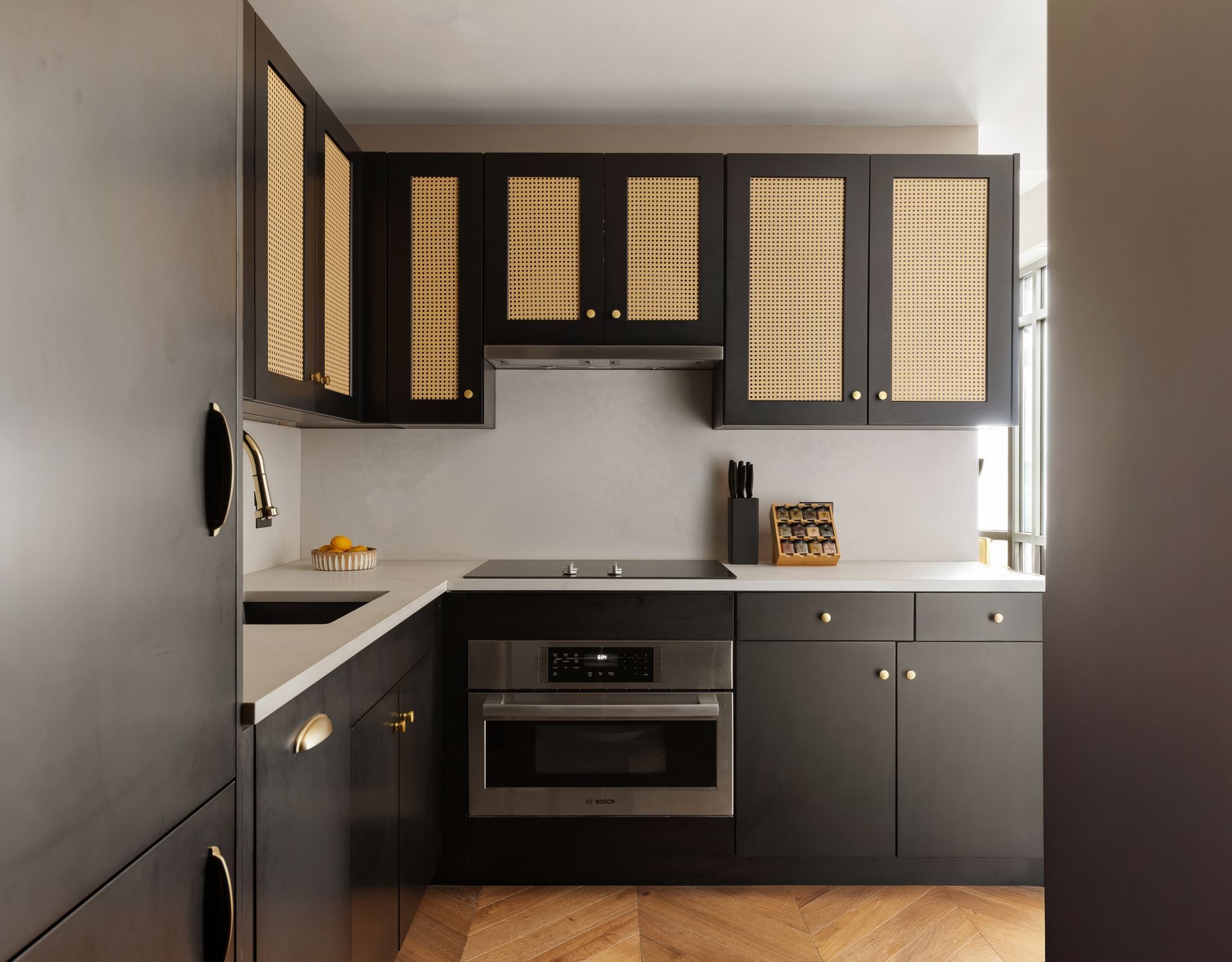 Modern kitchen with black cabinets and woven cabinet inserts, light countertops, and wood floors.