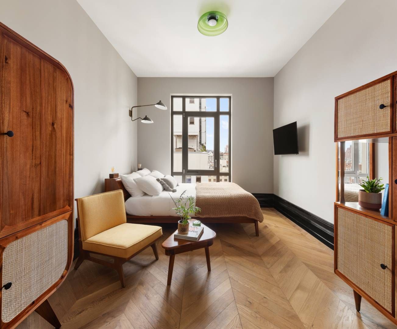 Bedroom with wooden furniture, bed, small table, and a window, featuring a light color scheme and herringbone floors.