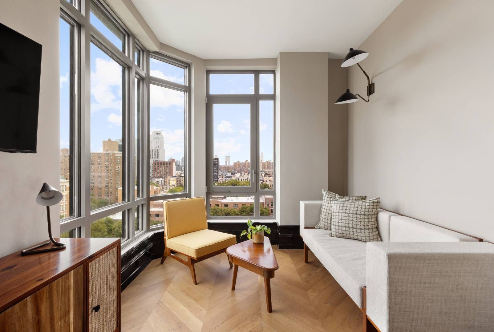 Bright living room with large windows, a sofa, yellow chair, and city view.