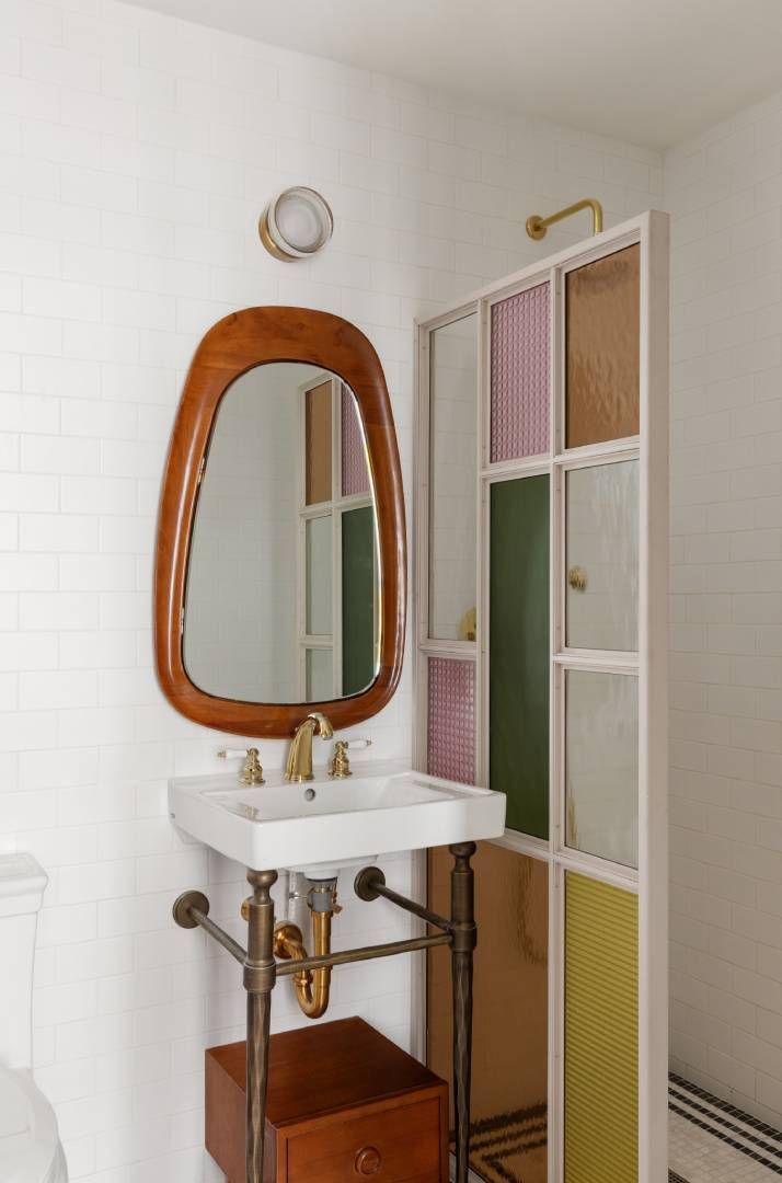 Bathroom with a wooden-framed mirror, white sink, and a colorful glass panel divider against a white brick wall.