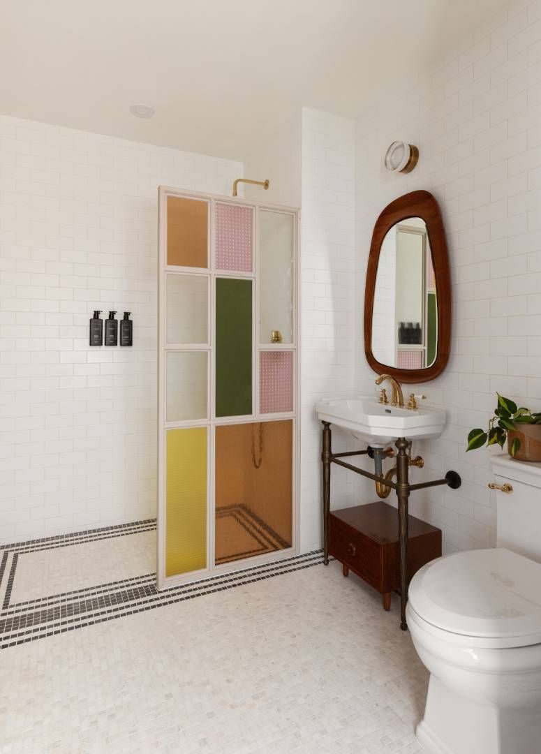 Bathroom with colorful shower screen, white tile, wood vanity, and an organic-shaped mirror.