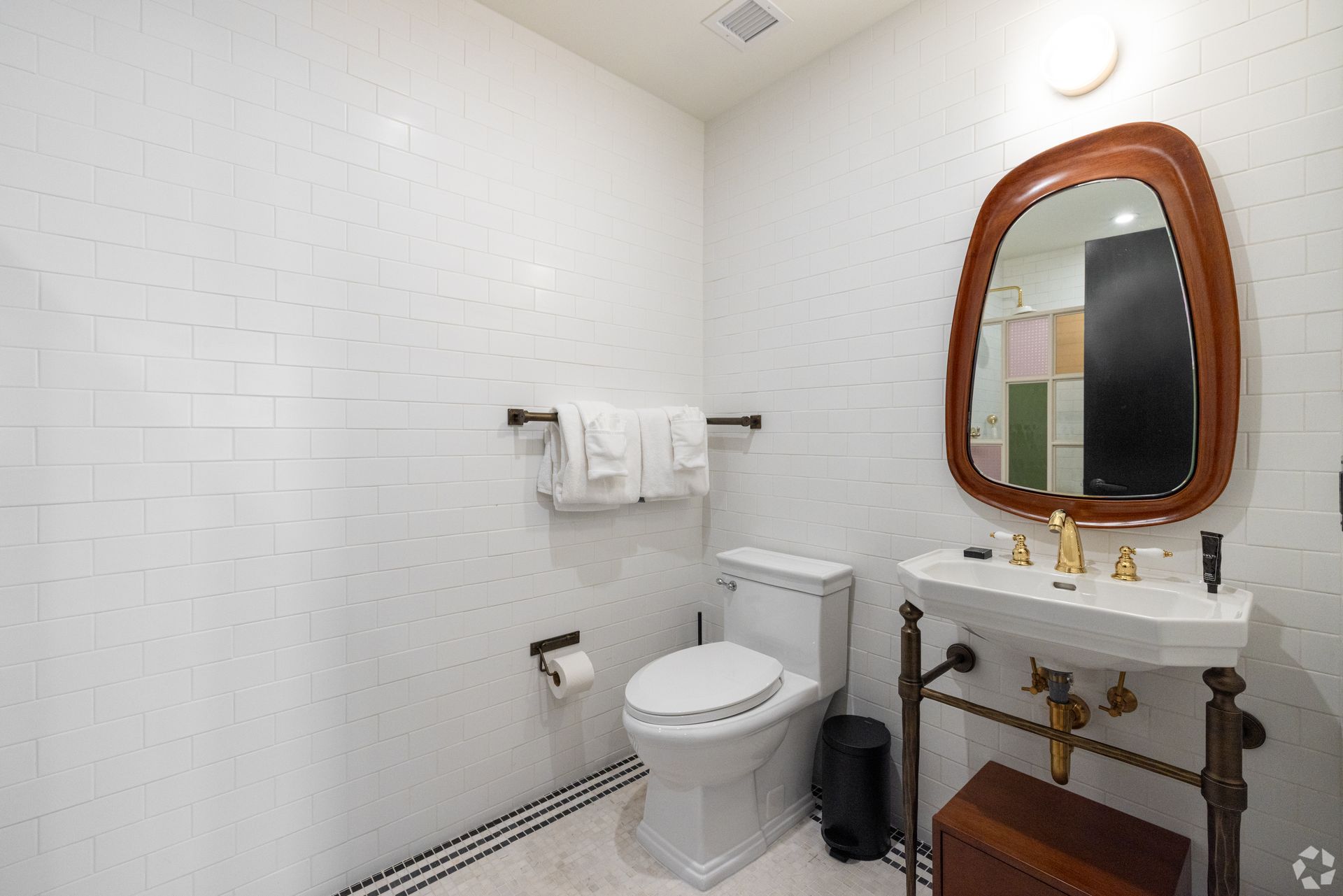 Bathroom with white tiled walls, toilet, vanity, and brown framed mirror. Towels hang on a towel bar.