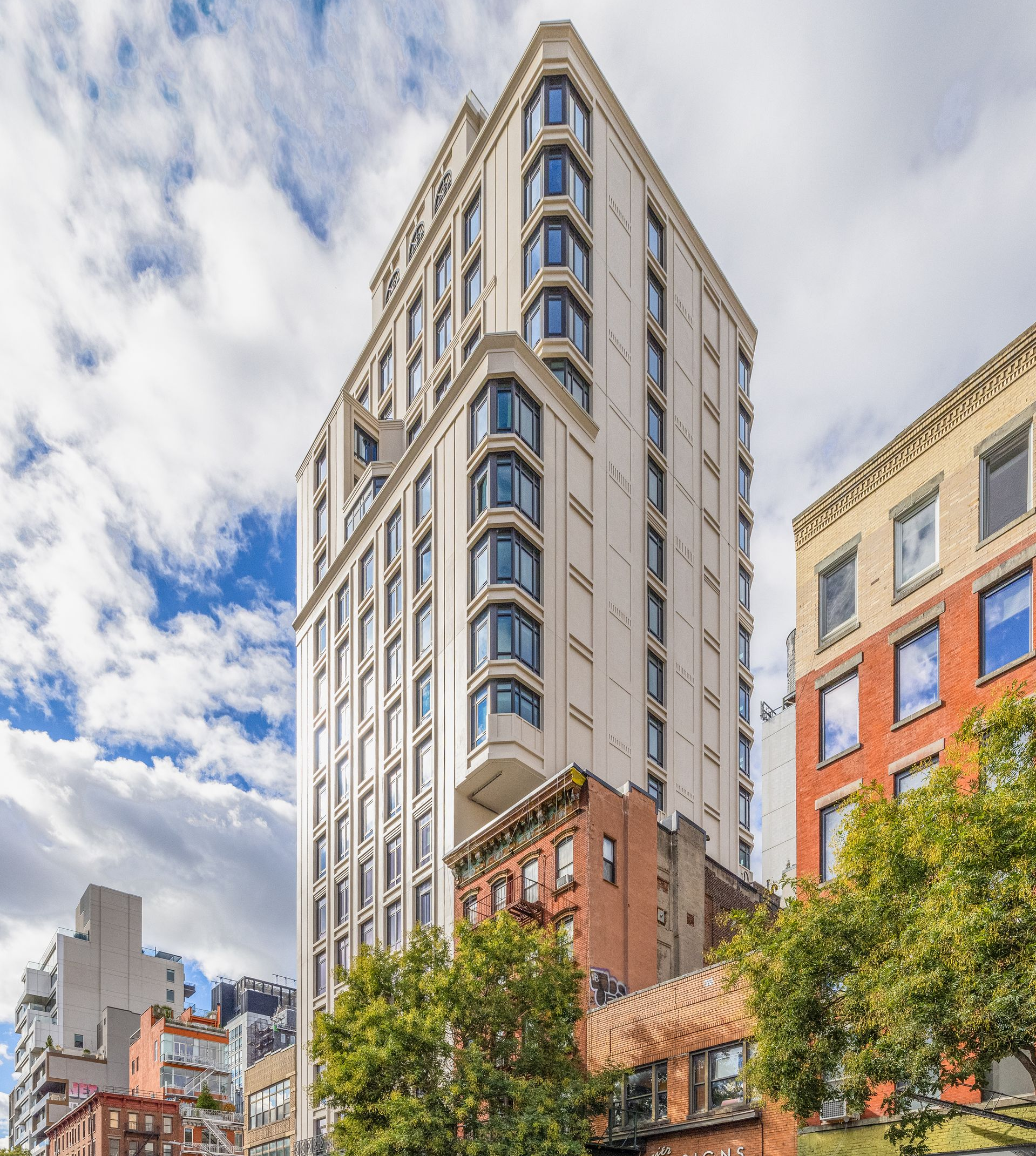 Tall, light-colored building with rounded bay windows amid smaller brick buildings and a blue sky.