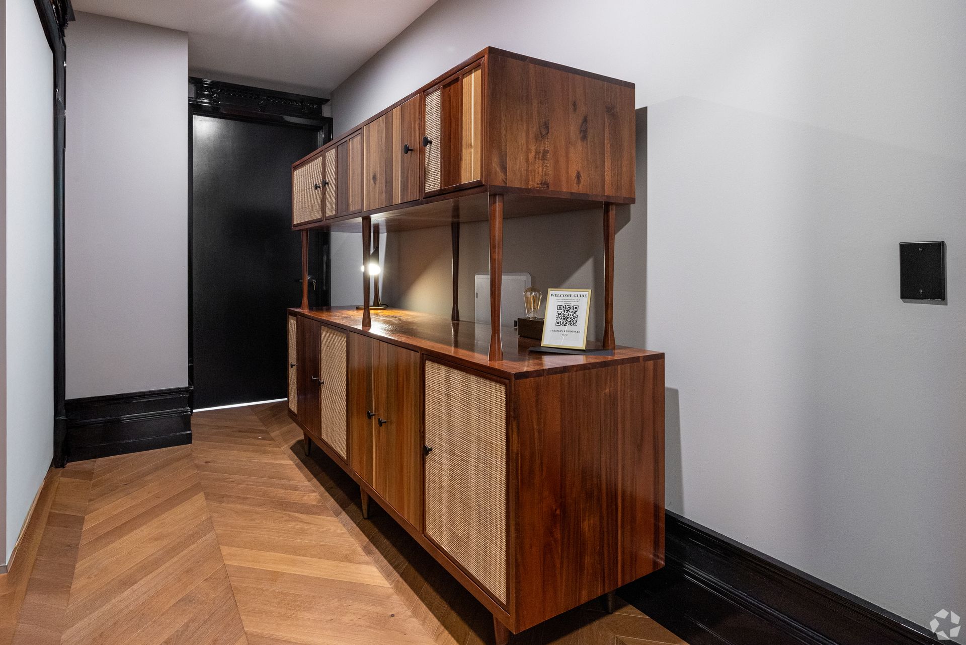 Wooden storage unit in a hallway with a black door, brown floor, and gray walls.