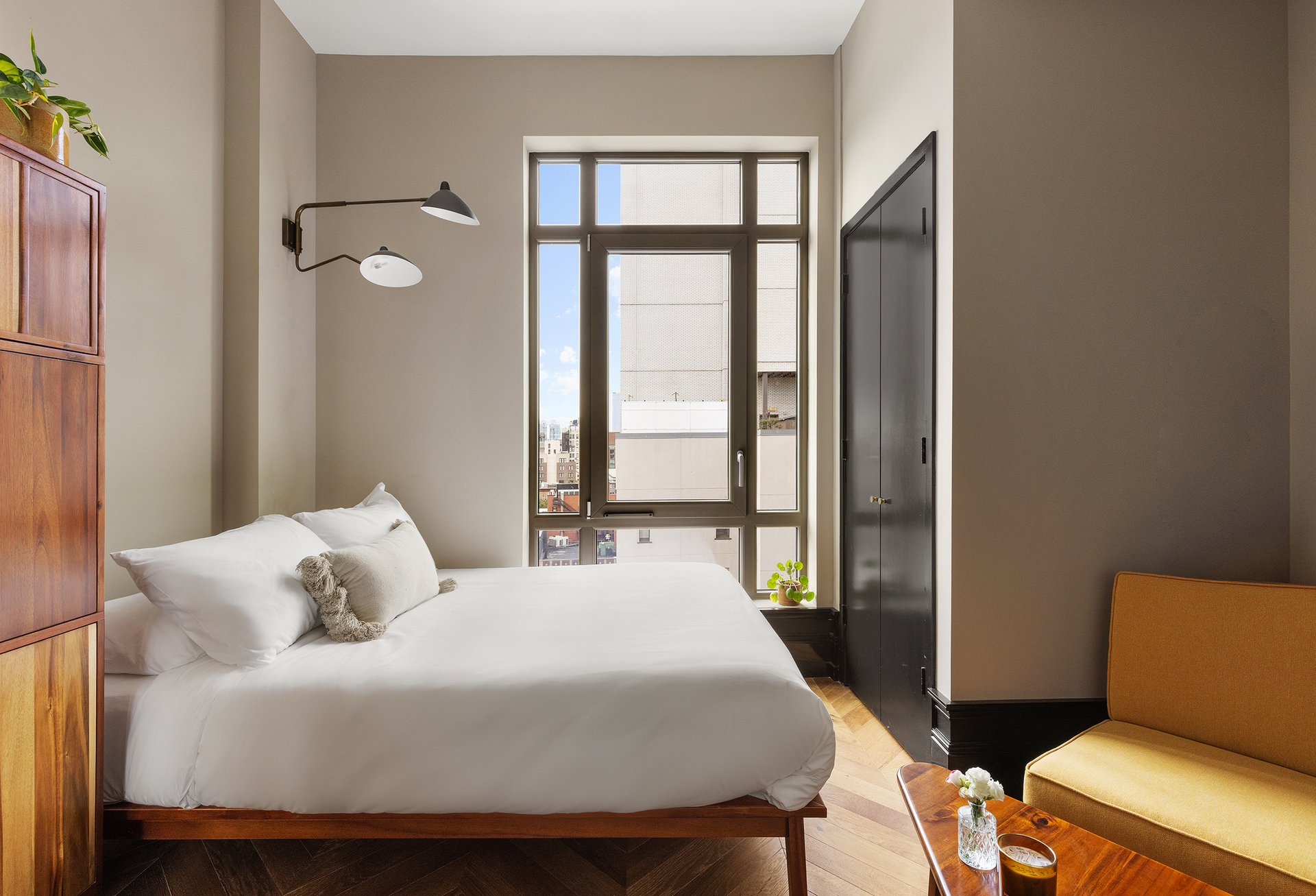 Bedroom with bed, tall wooden cabinet, window, black door, and yellow couch.