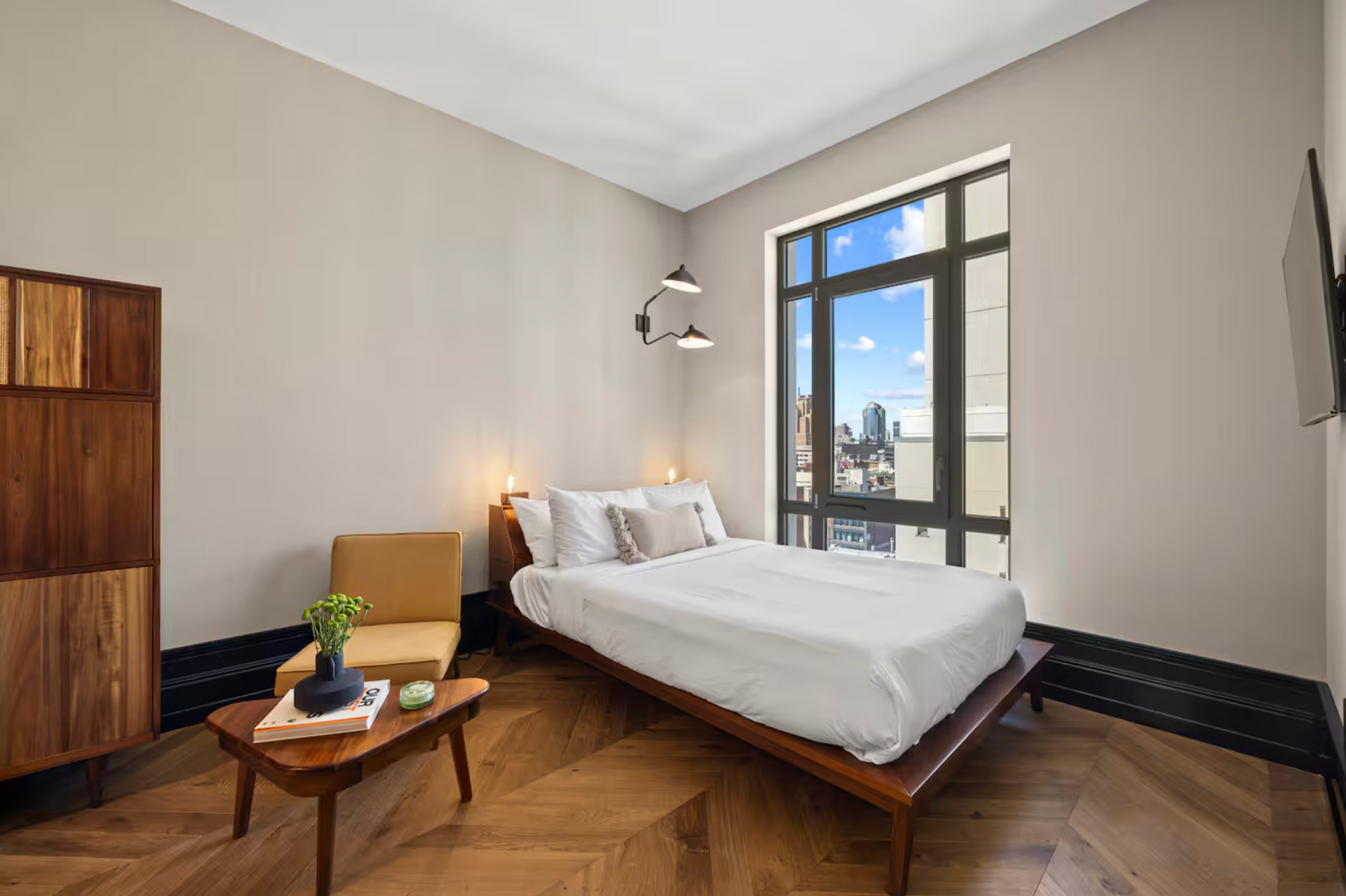 Bedroom with bed, chair, and wood furniture, large window with city view.