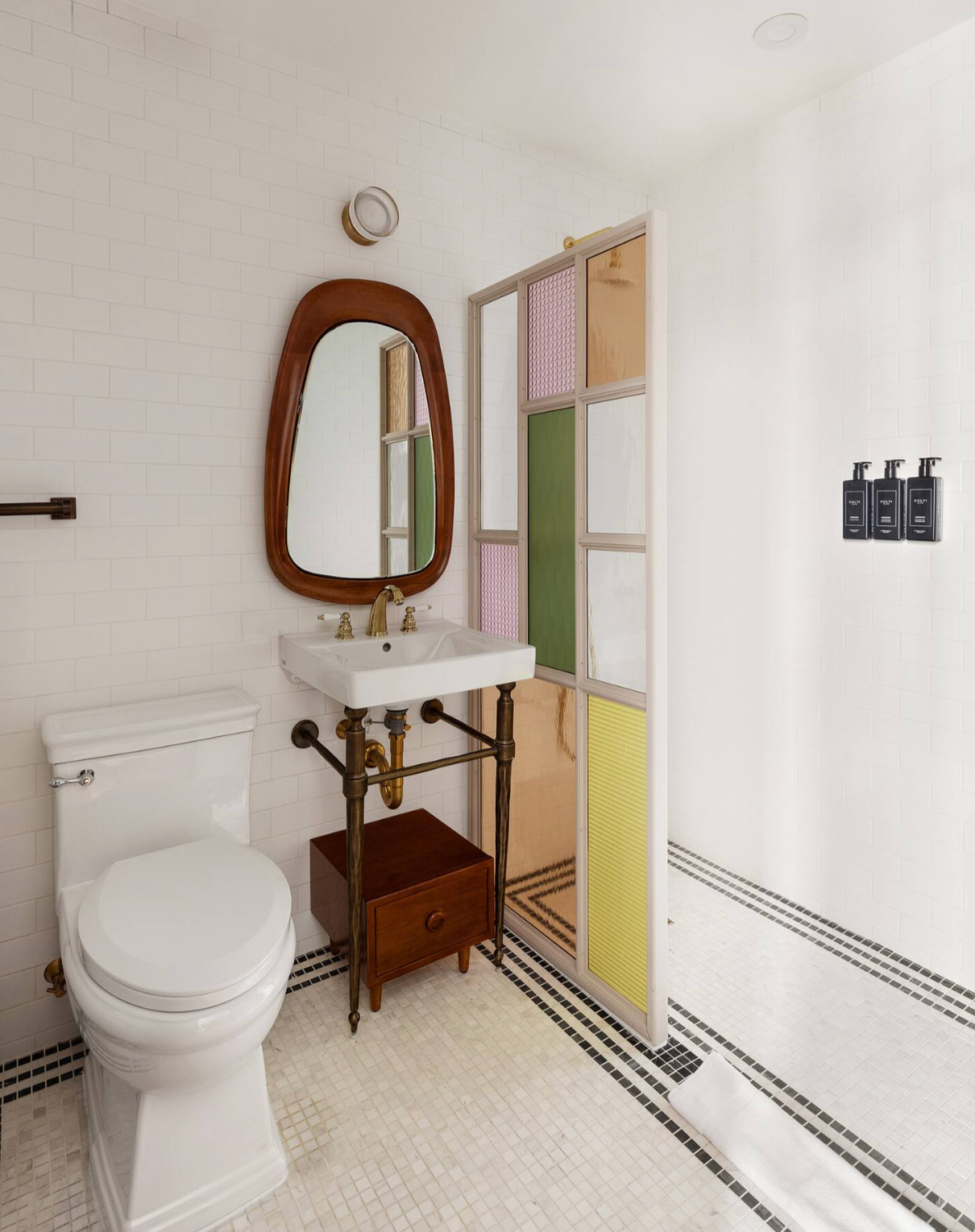 Bathroom with white walls, a colorful shower panel, and a wooden-framed mirror.