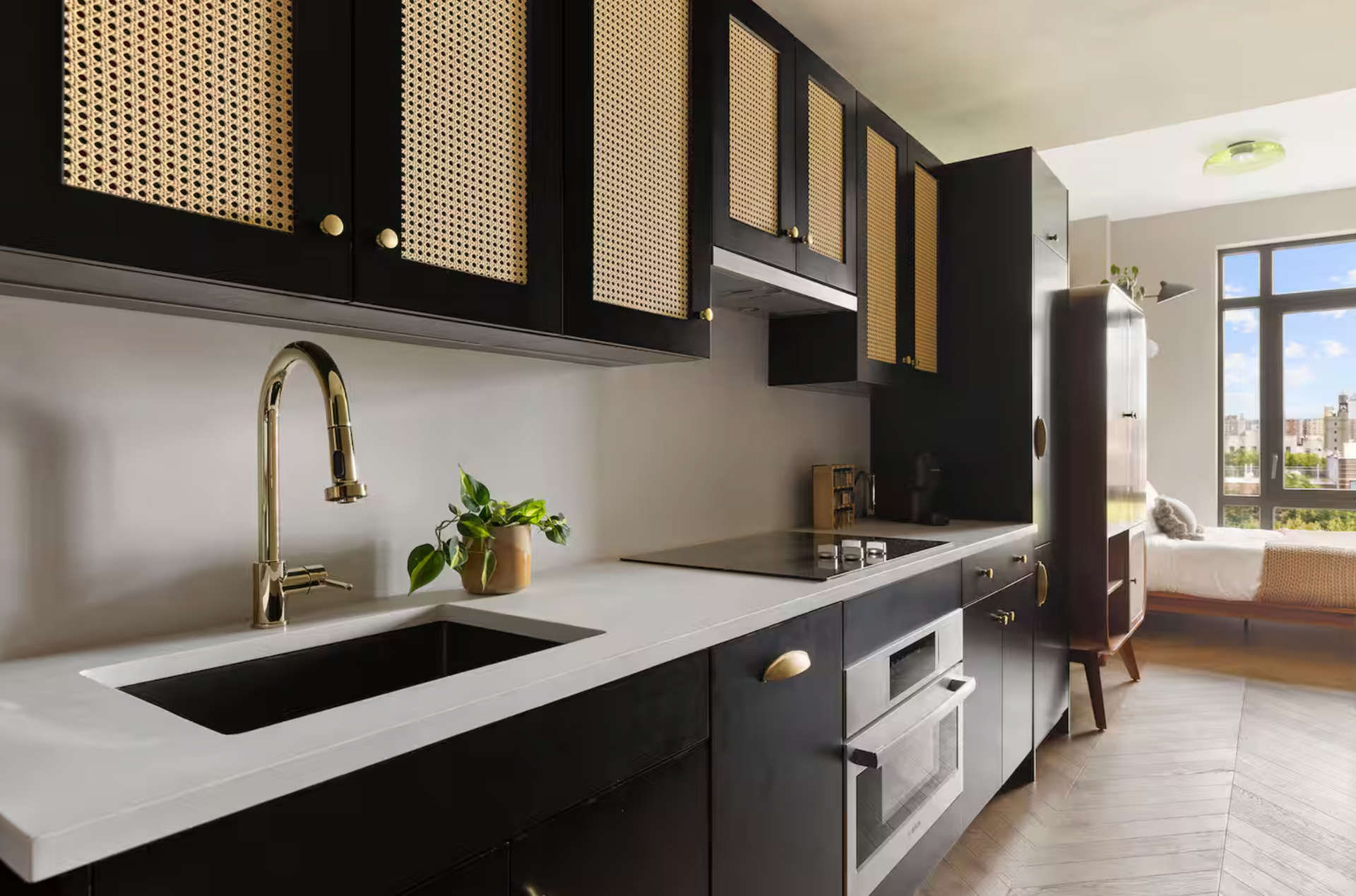 Modern kitchen with black cabinets, woven cabinet doors, white countertops, and gold faucet.