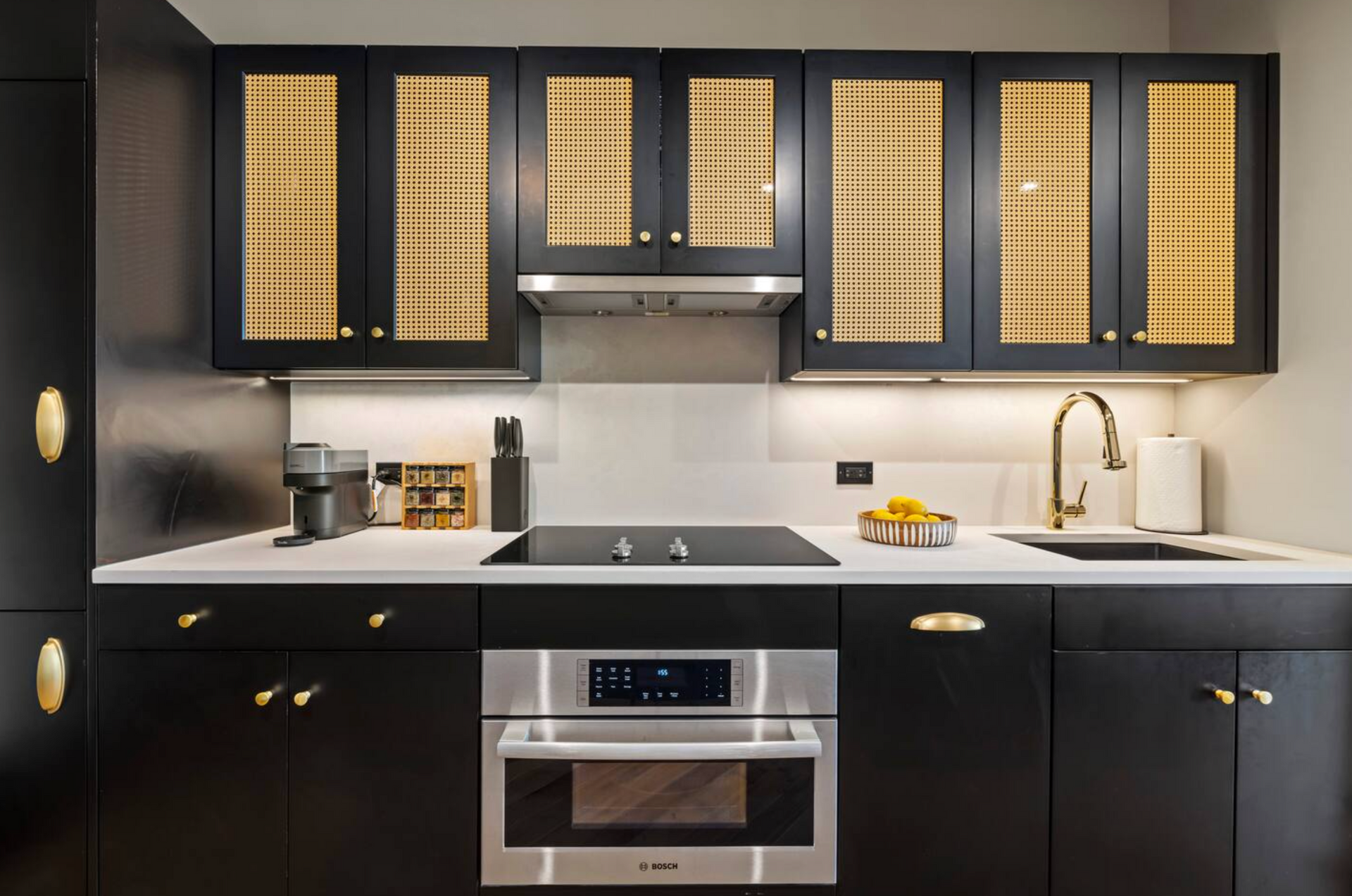 Black and gold kitchen cabinets with integrated appliances, gold hardware, and a white countertop.