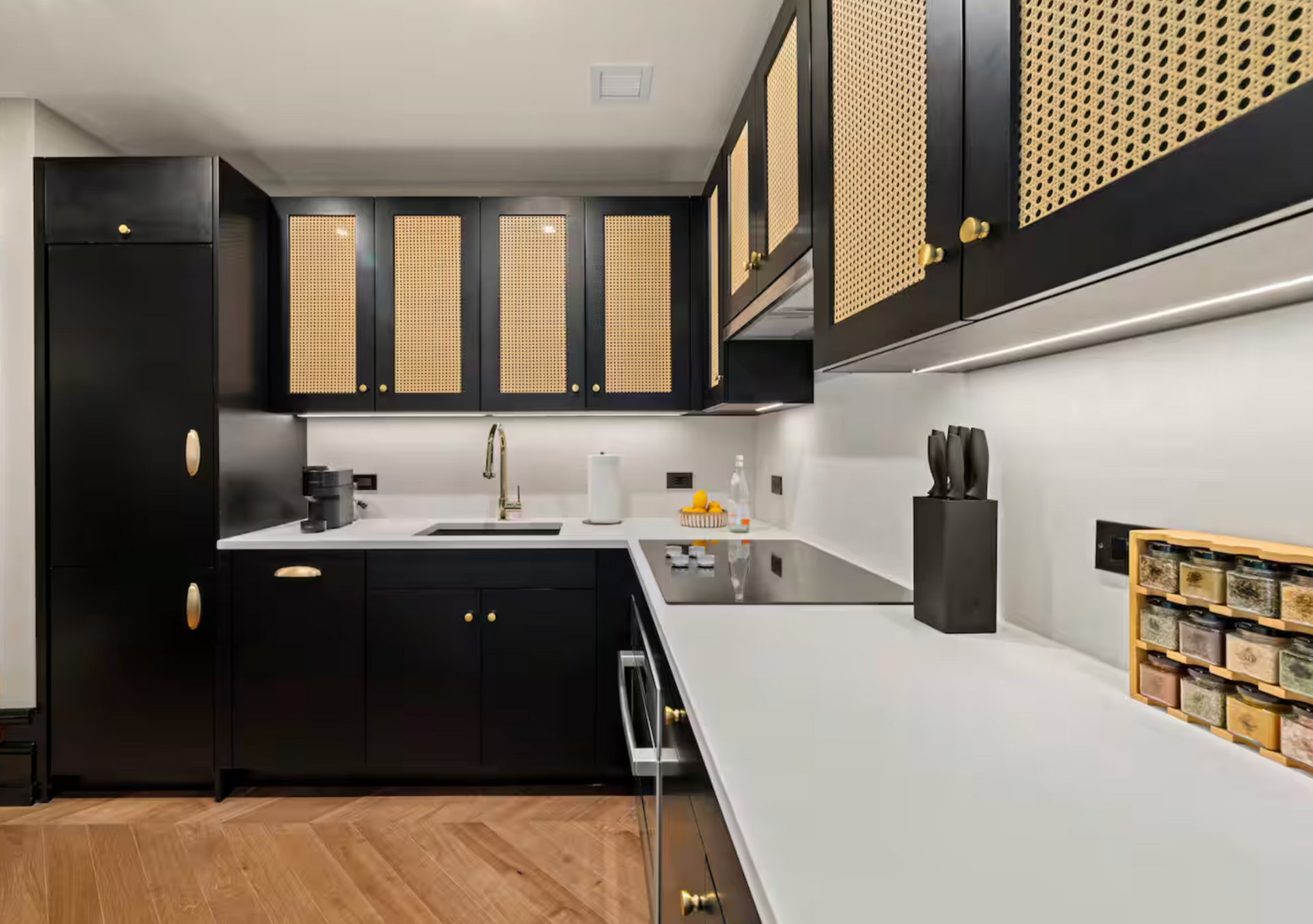 Black kitchen with rattan cabinet inserts, white countertops, and wooden floors.