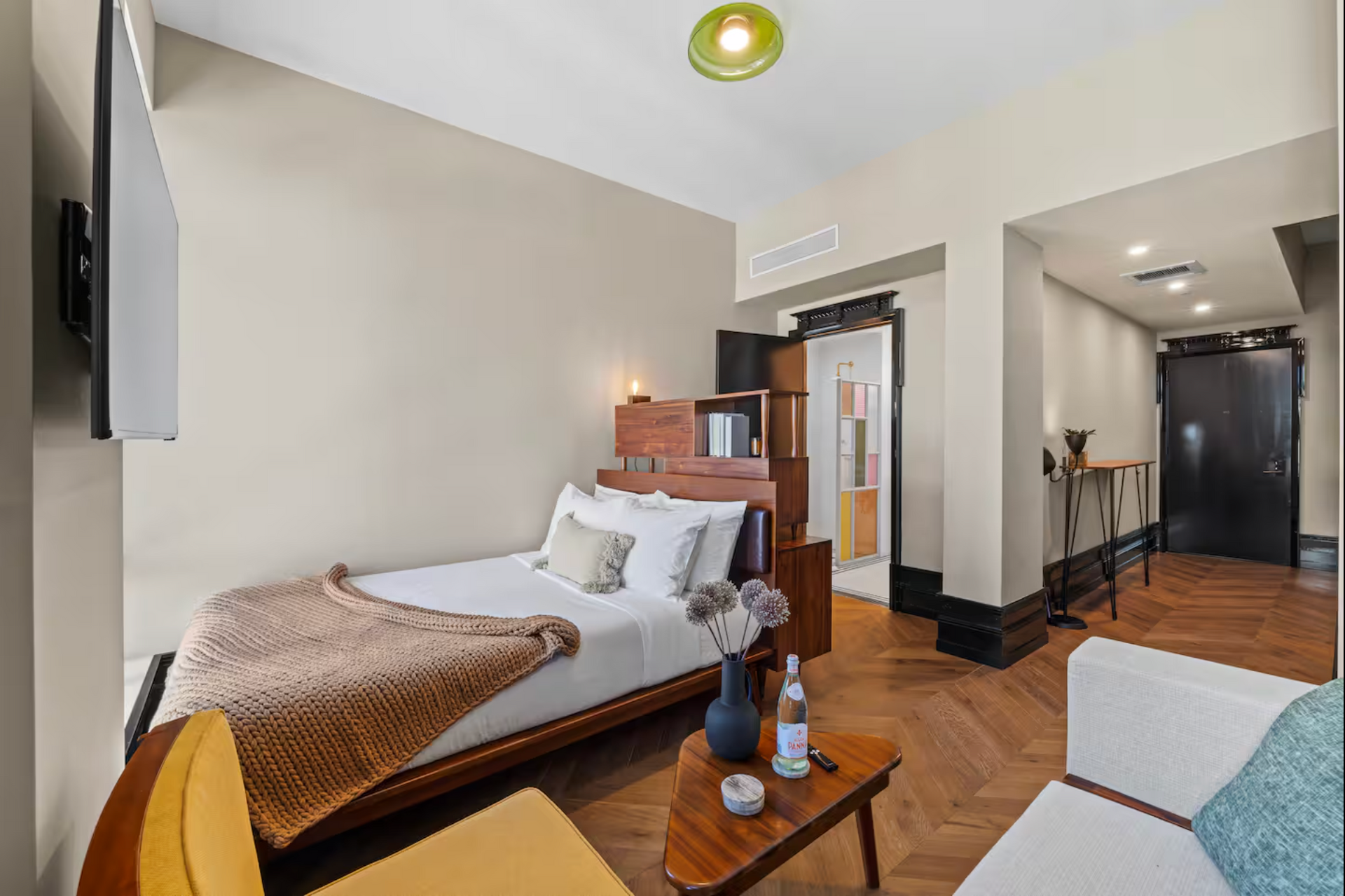 Small hotel room with a bed, small sofa, and a table. Wooden floor and tan walls.