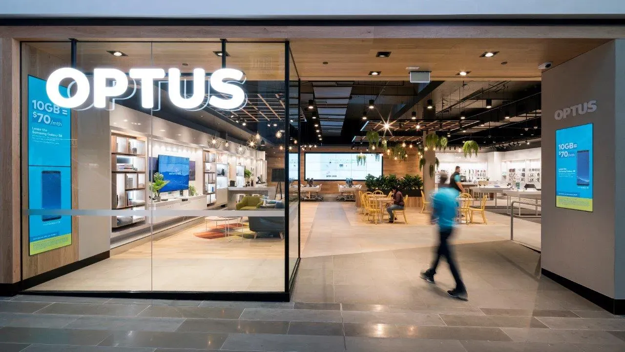 A man is walking in front of an optus store.