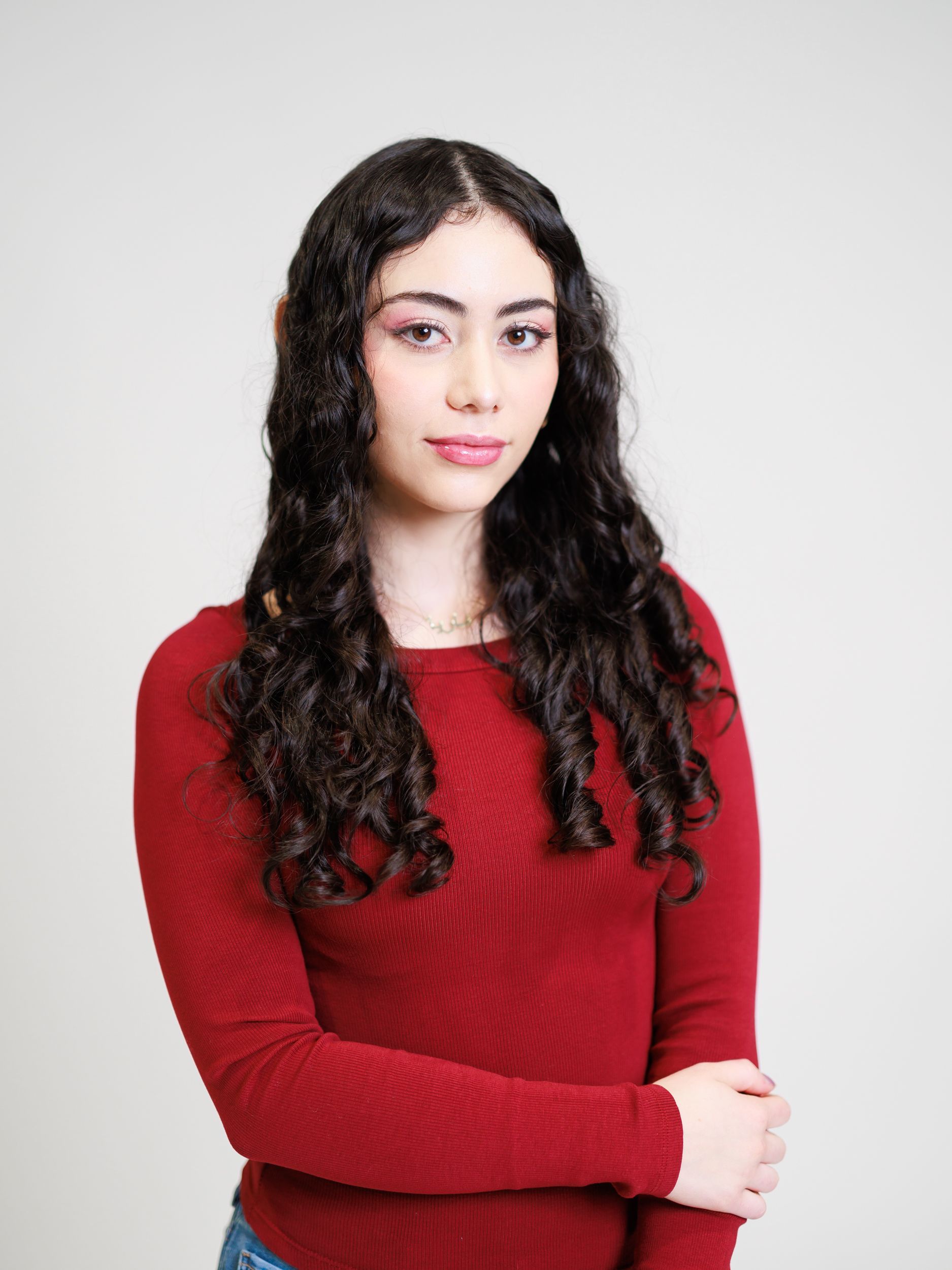 A young woman with long curly hair is wearing a red sweater and jeans. . Toronto Headshot Photography