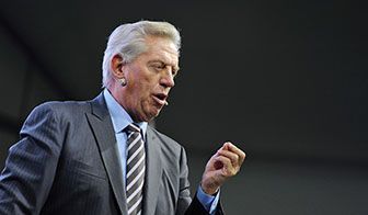 Man in suit, speaking, gesturing with hand. Gray hair, open mouth, light skin.