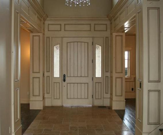 Interior view of a doorway with columns and side windows, painted white with gold trim, leading into a home.