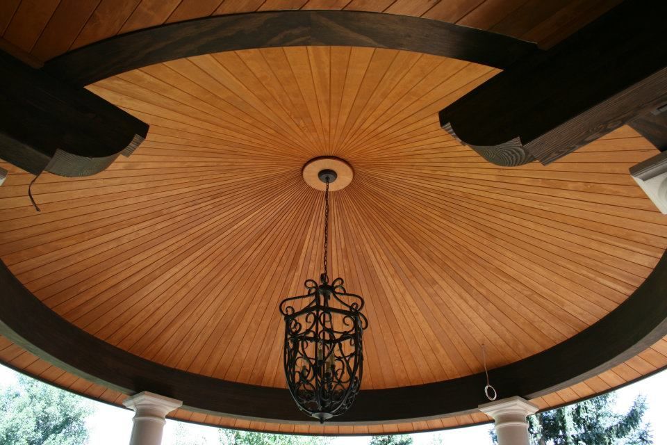 Wooden, radial ceiling with a decorative chandelier hanging in an outdoor, covered space.