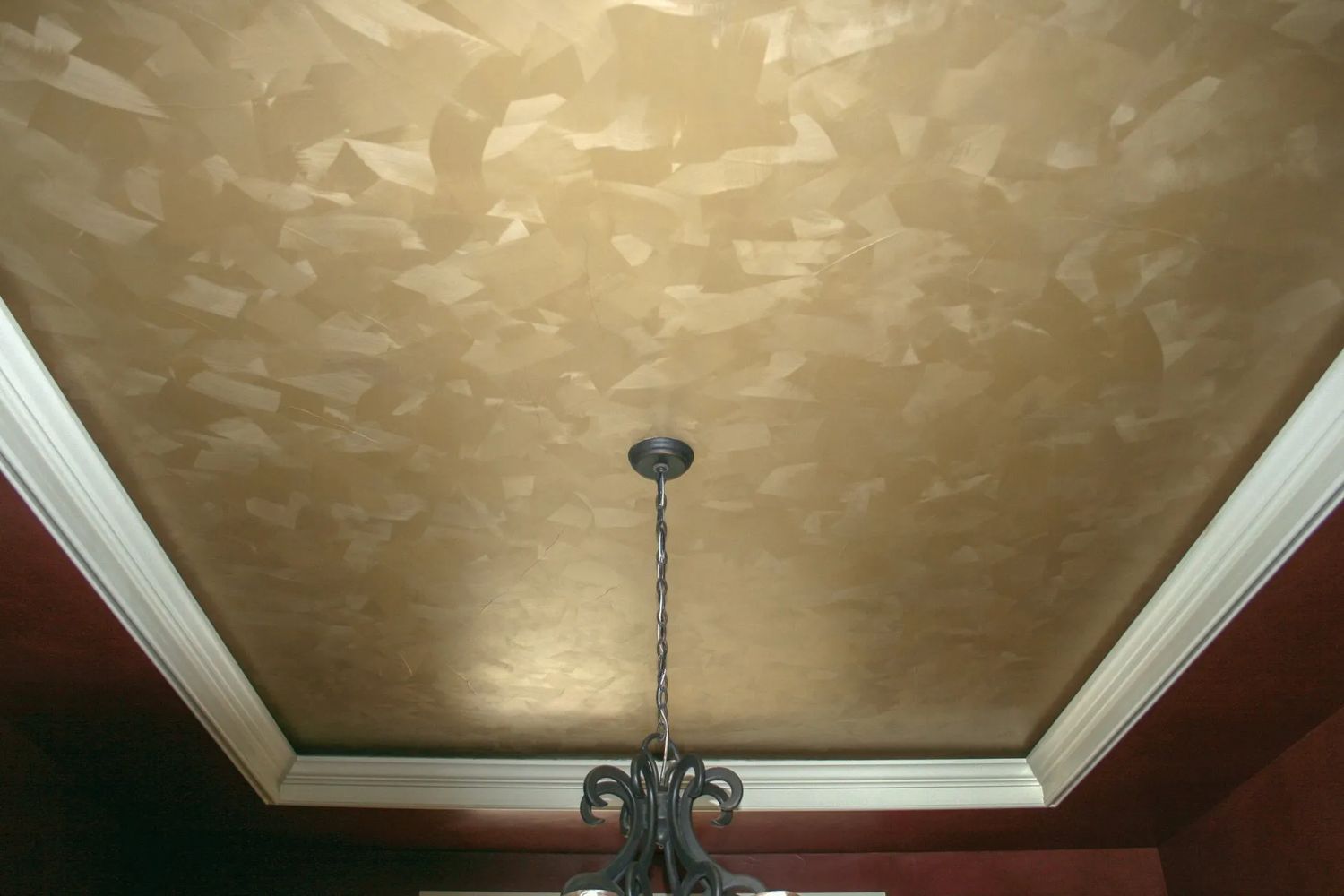 Gold-colored, textured ceiling with white trim and a chandelier. Red walls.