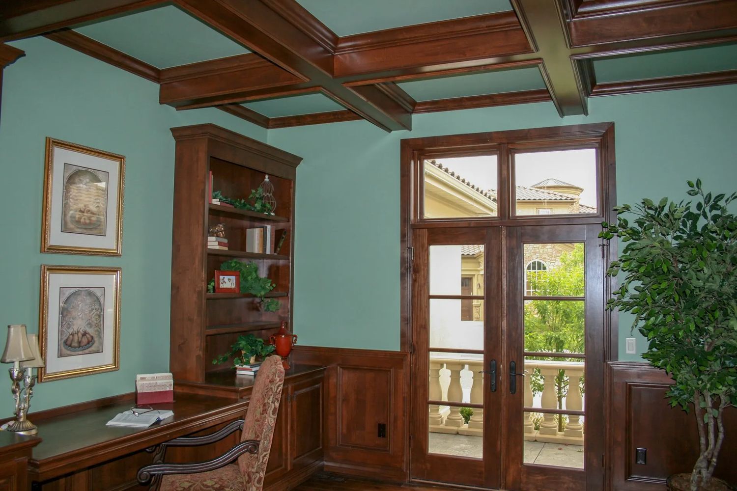 Study with teal walls, wood beams, built-in desk and bookshelf, double doors to balcony.