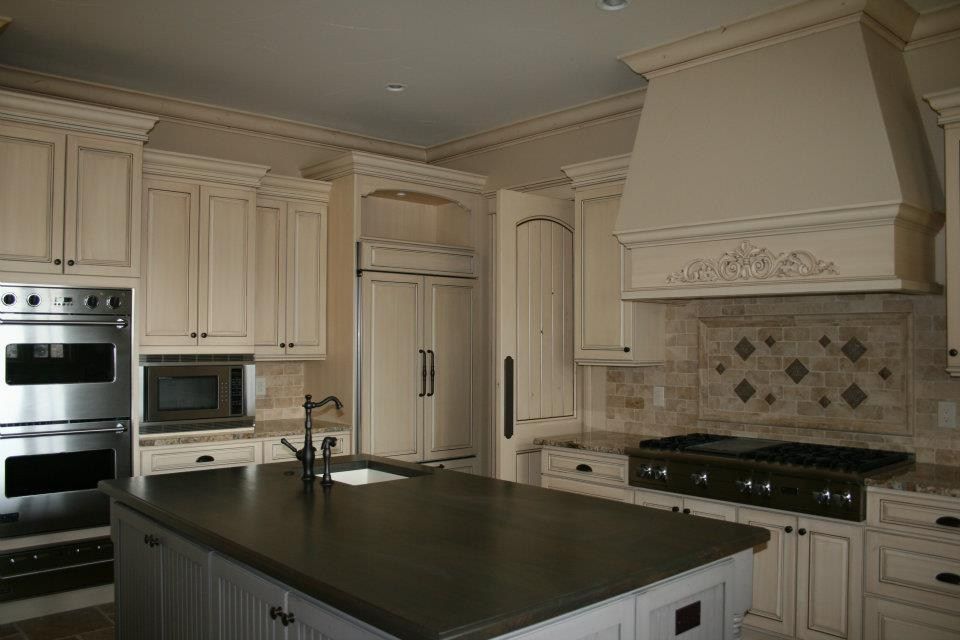 Cream-colored kitchen with an island, cabinets, oven, range, and refrigerator. Brown countertops and backsplash.