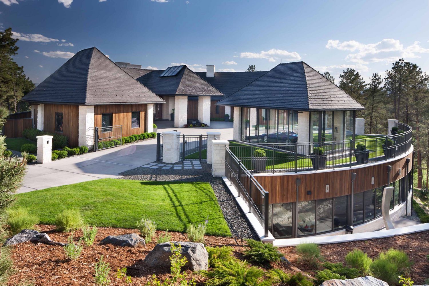 Modern house with curved glass wall, multiple peaked roofs, and landscaped yard.