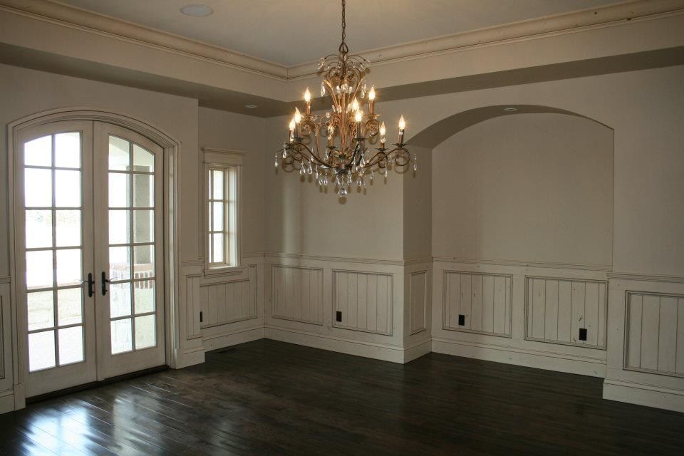 Formal dining room with dark wood floors, white walls with wainscoting, and a crystal chandelier.