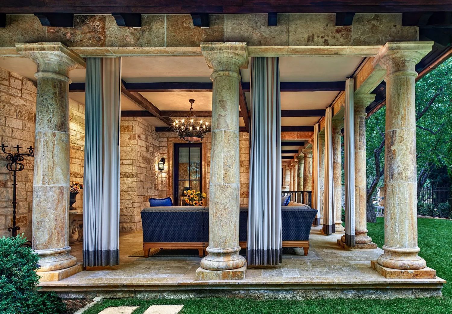 Stone columns support a covered patio with sofas and curtains.