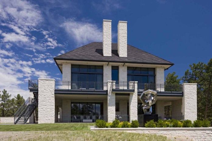 Modern two-story house with stone facade, balcony, and large windows against a blue sky.