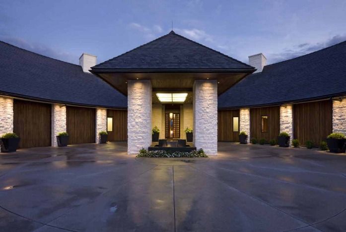 Modern home exterior with stone columns, dark roof, and water feature.