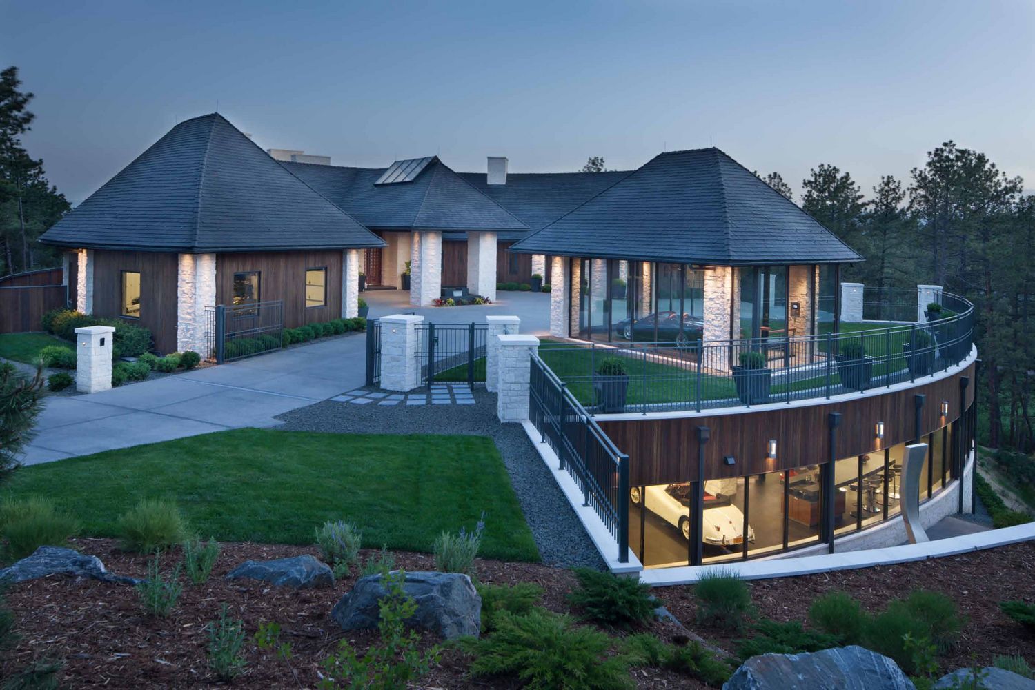 Modern house with curved glass wall, multiple rounded roofs, and a long driveway.