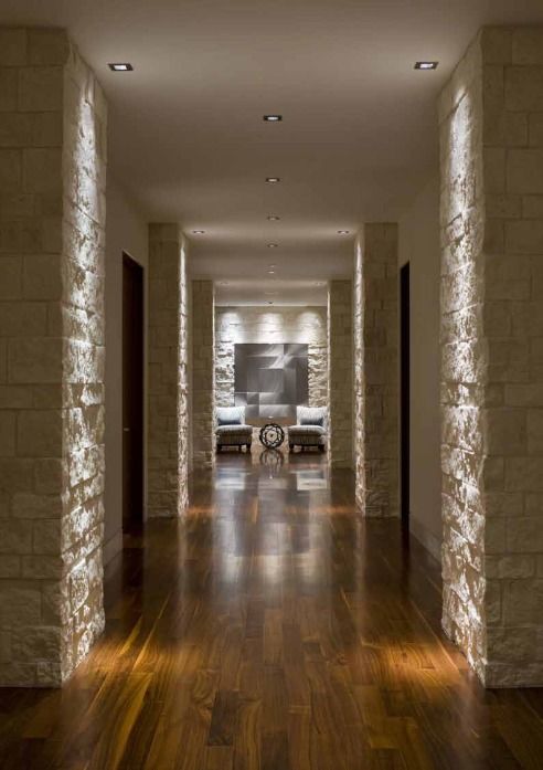 Hallway with wood floor, stone columns with recessed lighting, and artwork at the end.