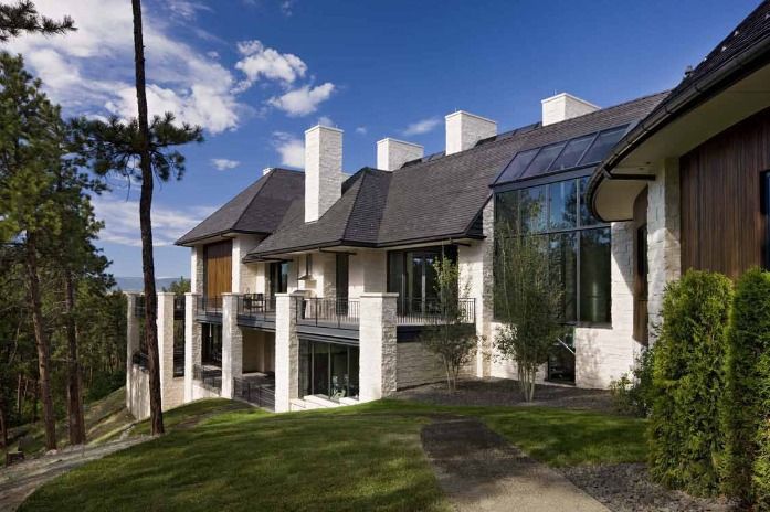 Luxurious multi-story home with stone and wood accents, grass lawn, and blue sky.