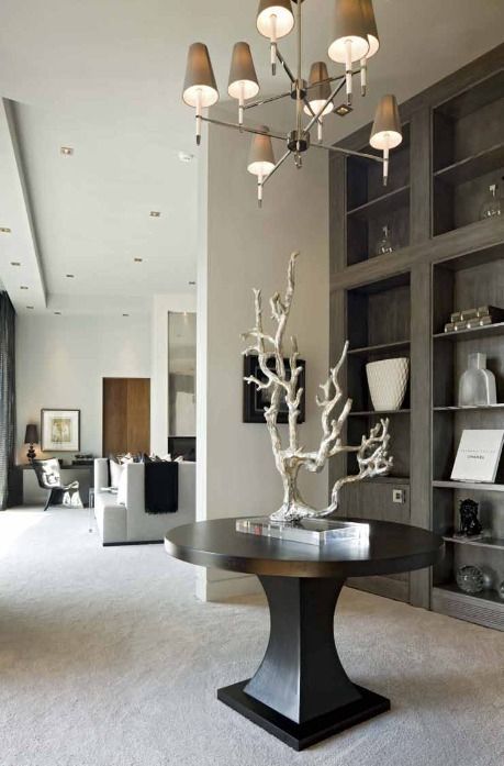 Elegant entryway with a round table, sculptural art, chandelier, and built-in shelves.