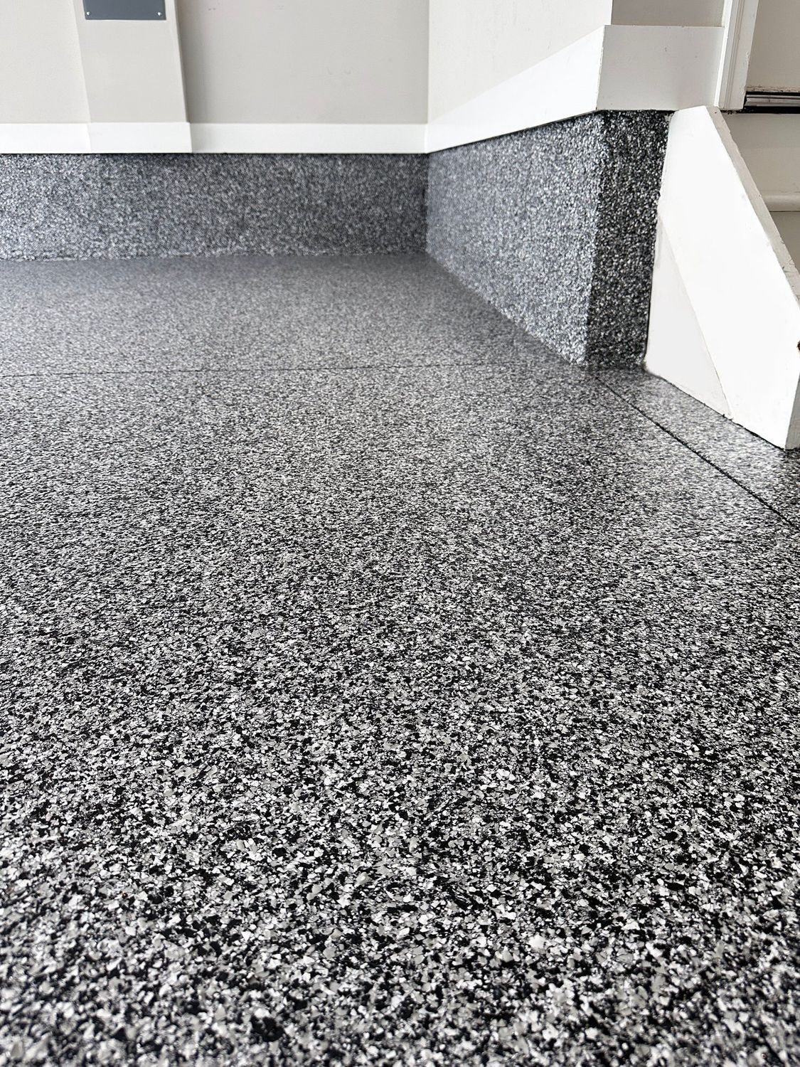 Gray speckled epoxy floor with matching baseboard in a corner of a room, under a white wall.