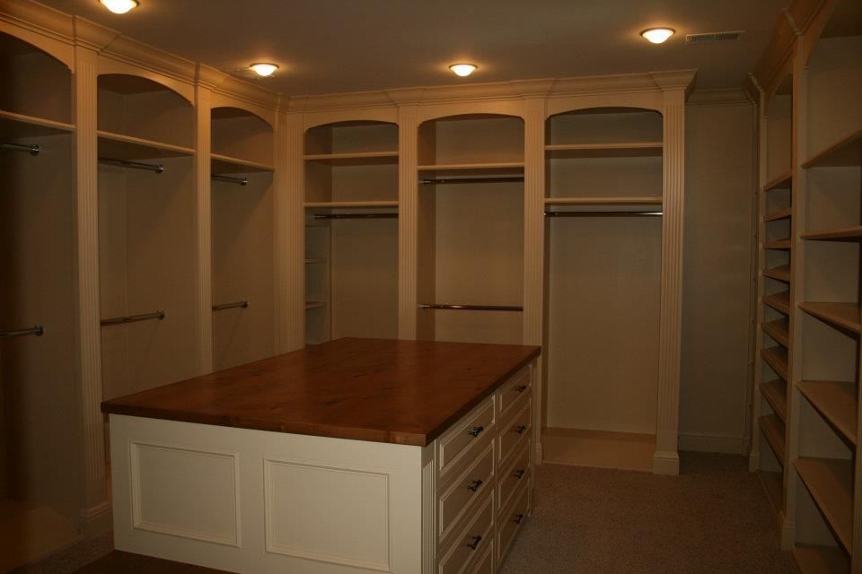 Walk-in closet with built-in shelves, hanging rods, and a center island with drawers. Neutral tones, overhead lighting.
