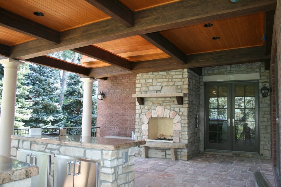 Covered patio with a stone fireplace, brick walls, and a wood beam ceiling.