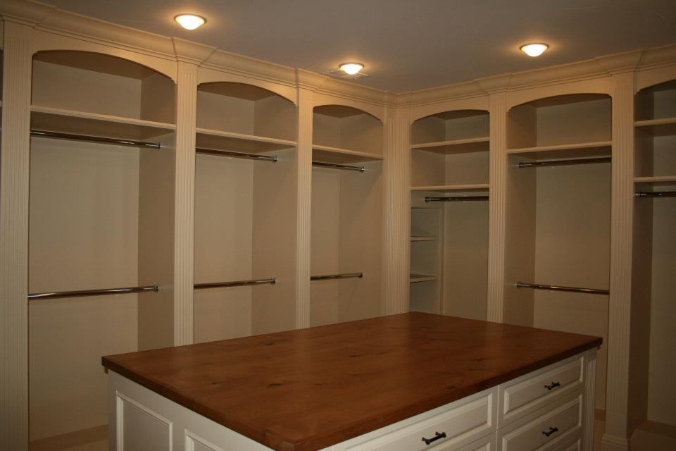 Empty walk-in closet with built-in shelves and rods, island with drawers, and wood countertop.