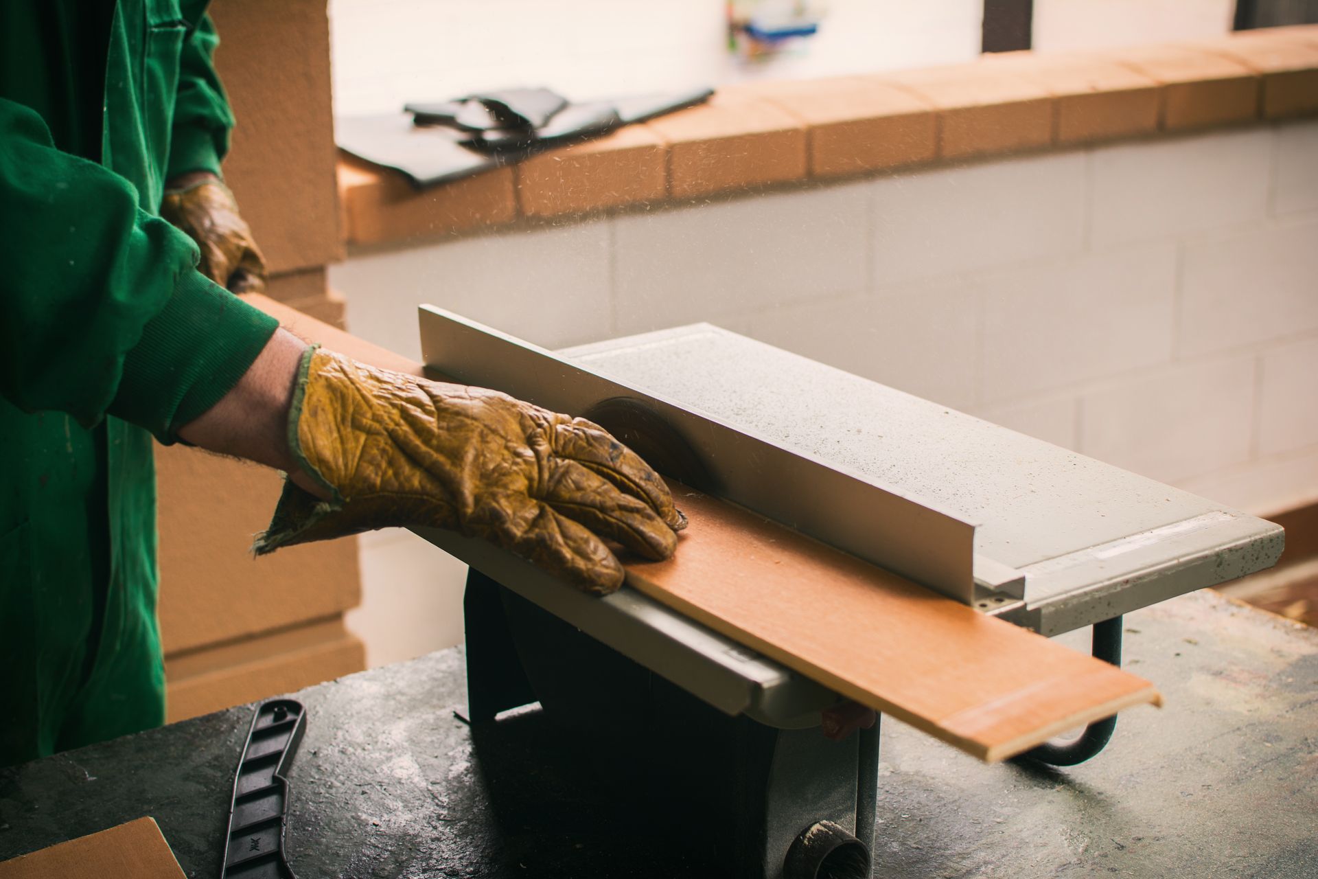 Person in green shirt and work gloves uses a table saw to cut a wooden plank.